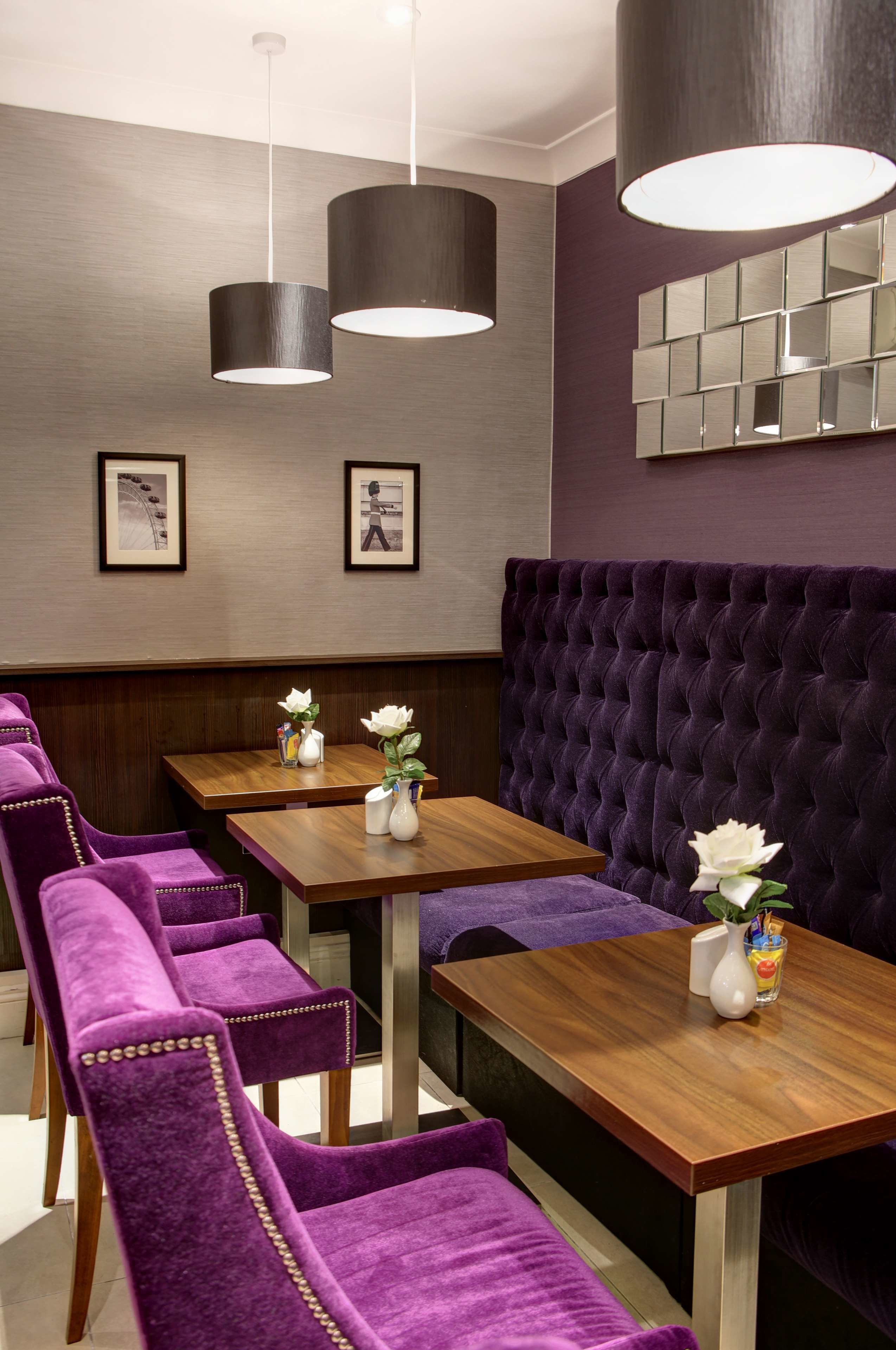 A restaurant with purple velvet chairs, wooden tables, and a tufted purple booth.
