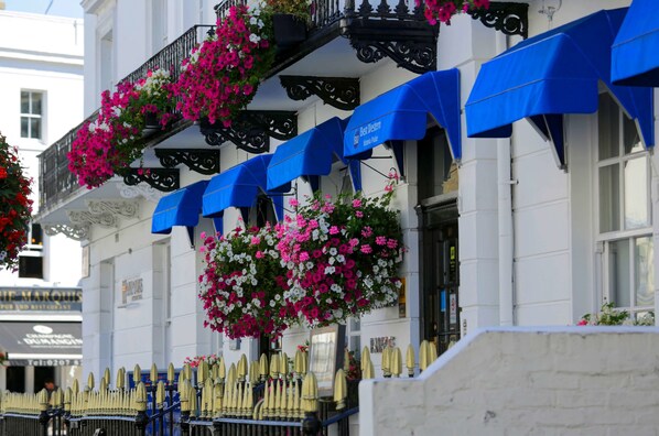 Un edificio con balconi decorati da cesti di fiori pensili e tende parasole blu.