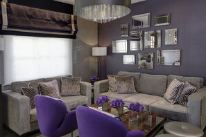 Un soggiorno moderno con un divano grigio, poltrone viola, un tavolino in vetro con fiori viola e un'ampia parete specchiante.