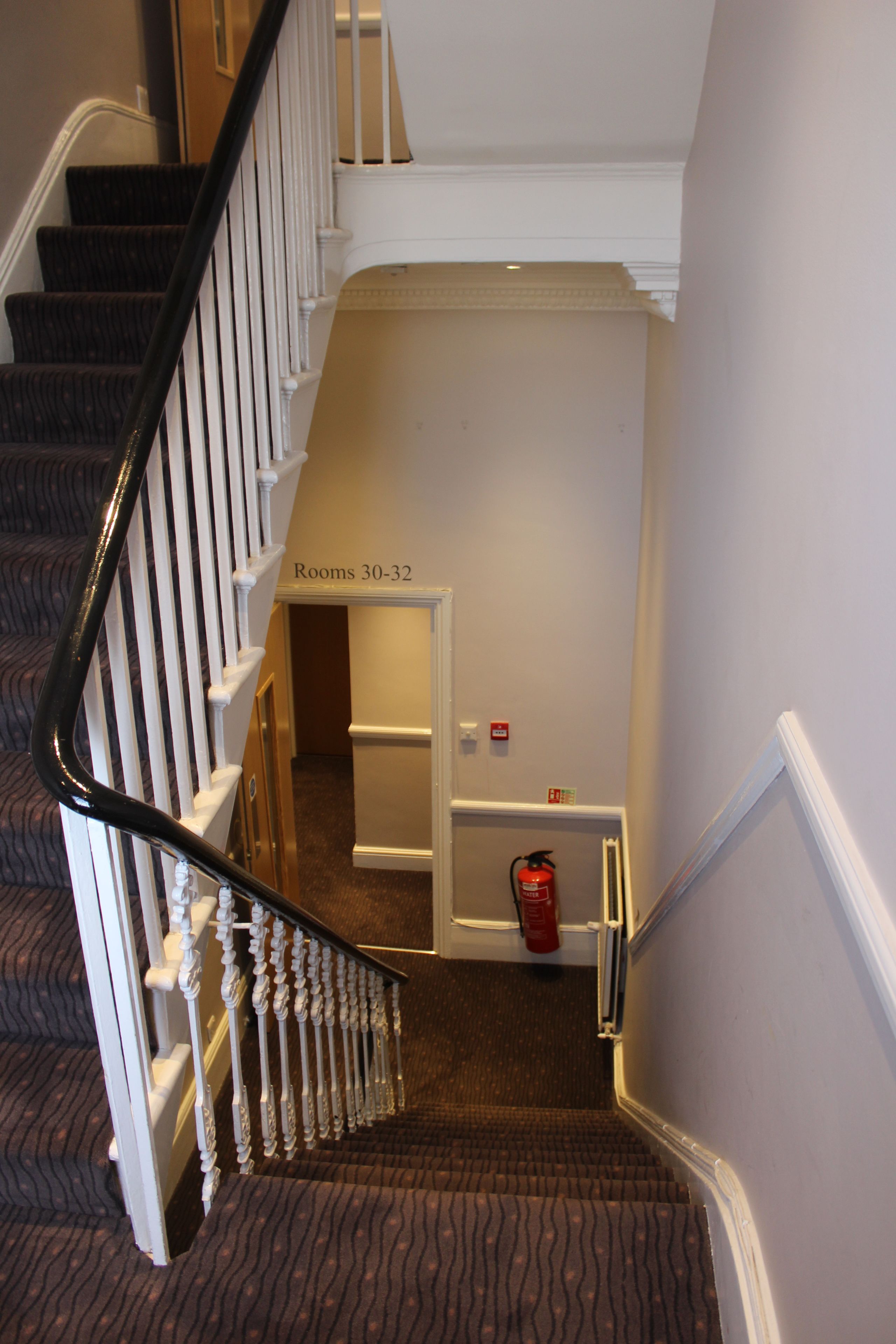A staircase with a carpeted floor and a fire extinguisher near the bottom.