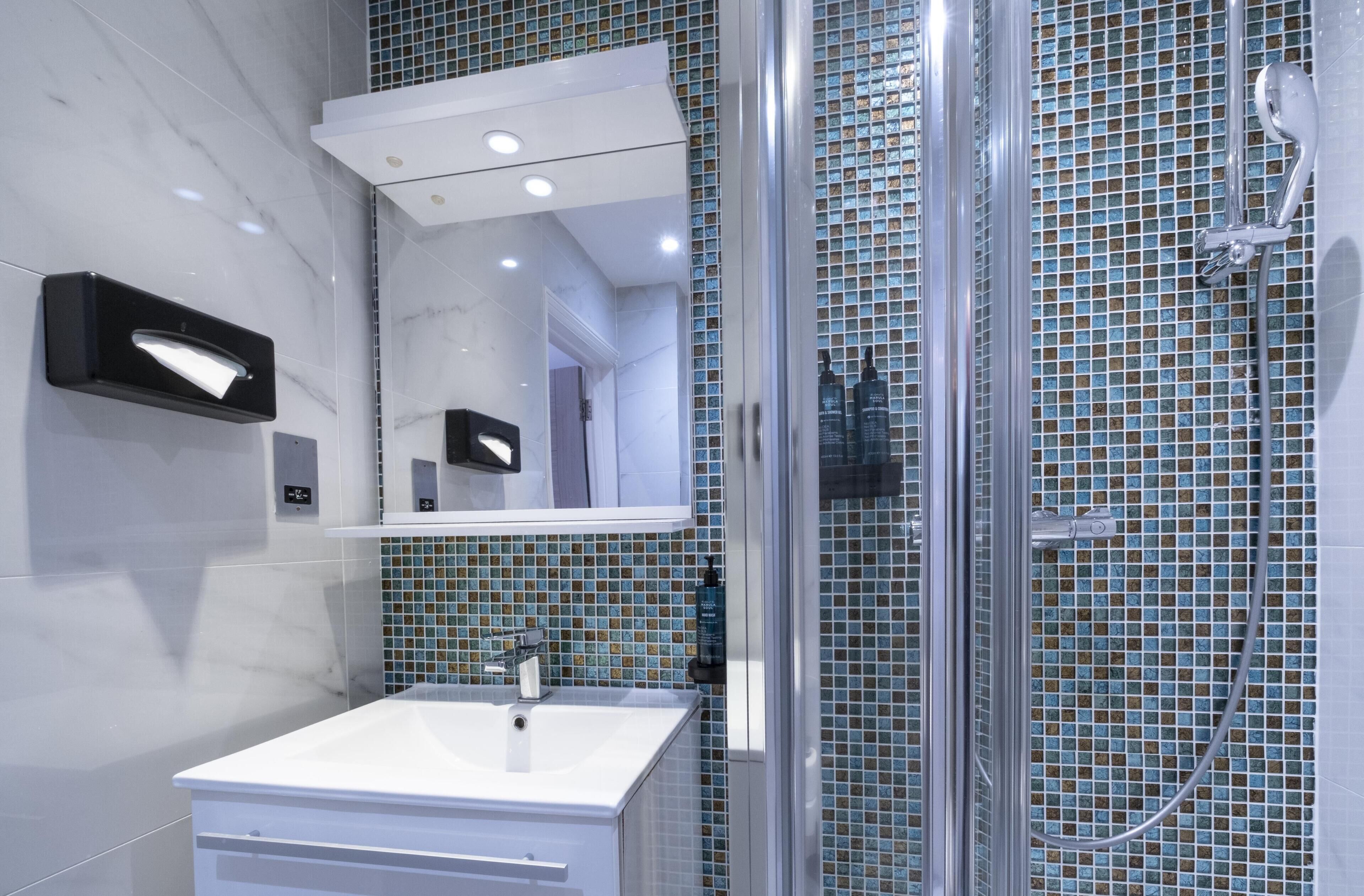 A modern bathroom with a glass shower enclosure, a white sink, and a tiled backsplash.