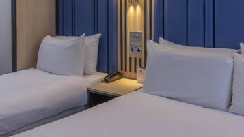 A hotel room with two beds, a bedside table with a phone, and a wall-mounted control panel.