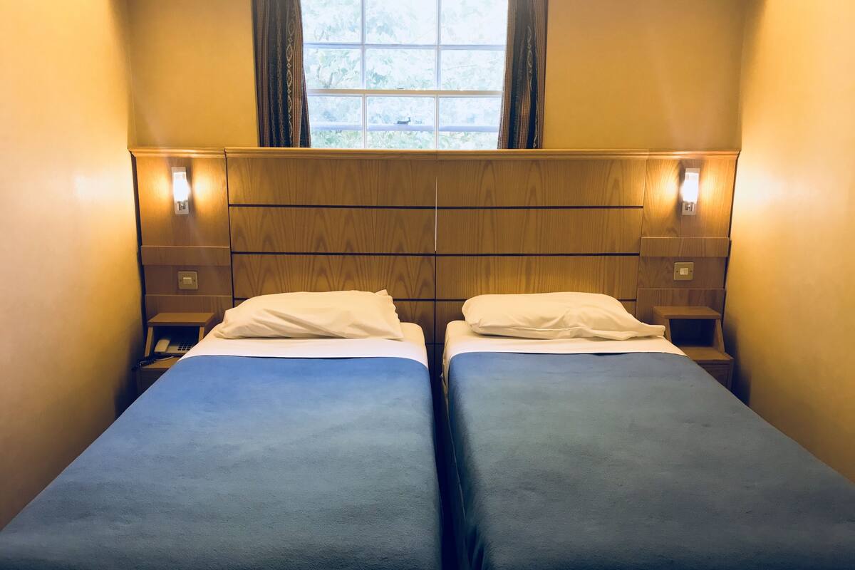 Habitación con dos camas individuales, cabeceros de madera, lámparas de noche y una ventana con cortinas.