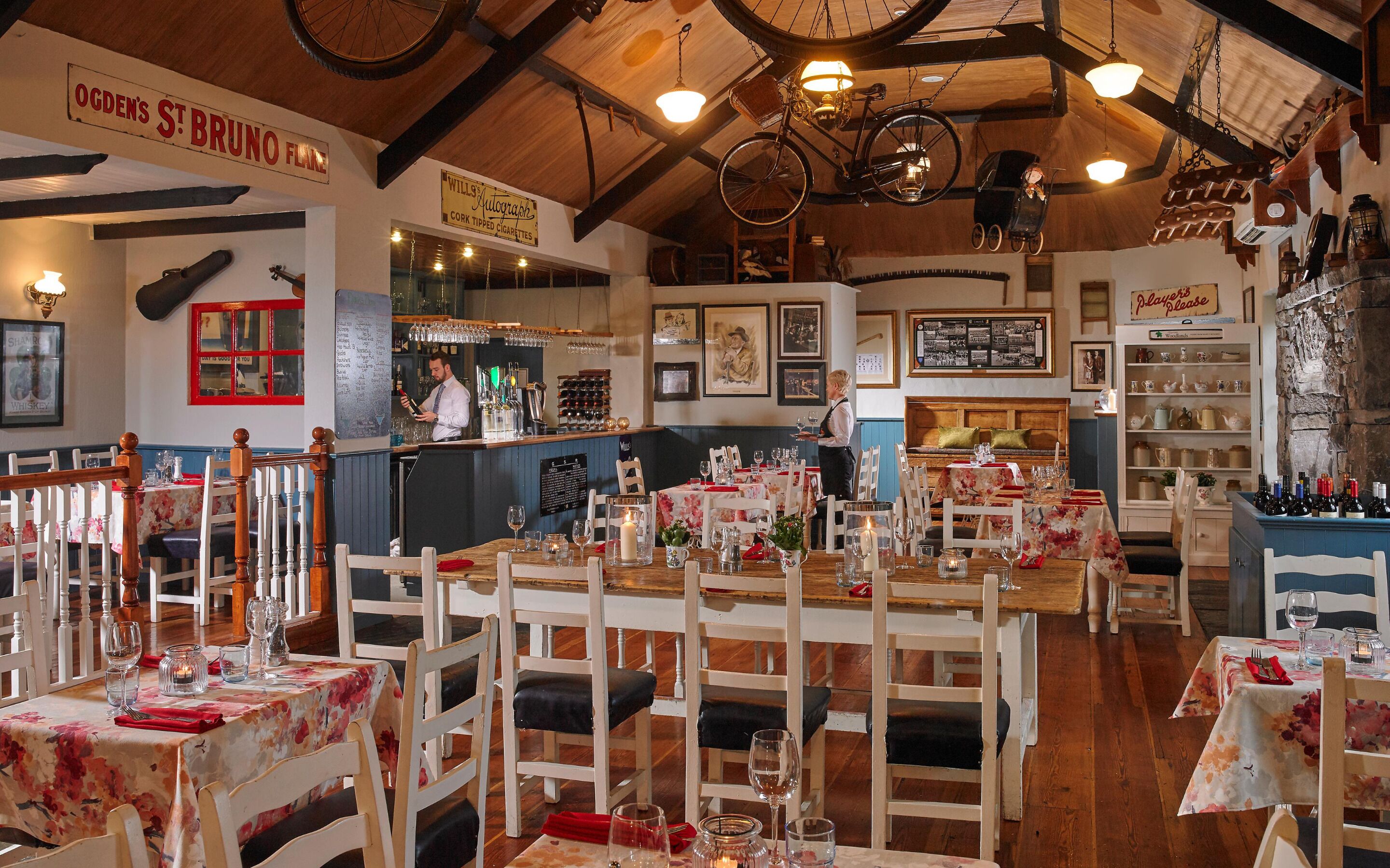 Un restaurante acogedor con mobiliario de madera, una zona de bar y diversas decoraciones, incluyendo una bicicleta y faroles.