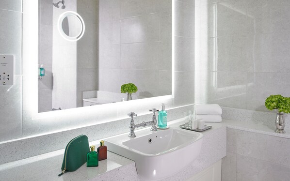 A modern bathroom with a white sink, a mirror with a light, and a small green plant.