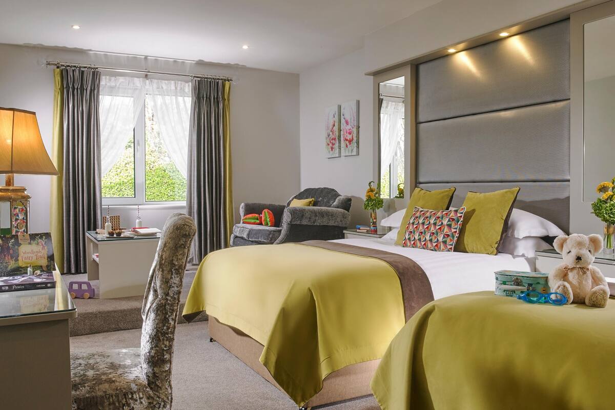 Ein Hotelzimmer mit einem großen Bett, einer Couch, einem Schreibtisch mit Lampe und einem Fenster mit Vorhängen.