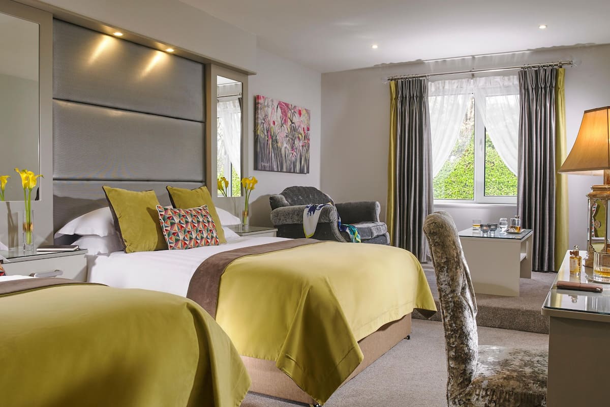 Ein Hotelzimmer mit zwei Betten, einem Schreibtisch mit Lampe, einem Stuhl und einem Fenster mit Vorhängen.