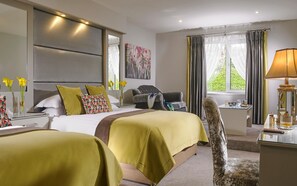 Quarto de hotel com duas camas, uma escrivaninha com abajur, uma cadeira e uma janela com cortinas.