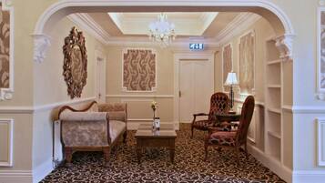 Un vestíbulo de hotel con alfombra estampada, un candelabro, un mostrador de recepción y decoraciones murales ornamentales.