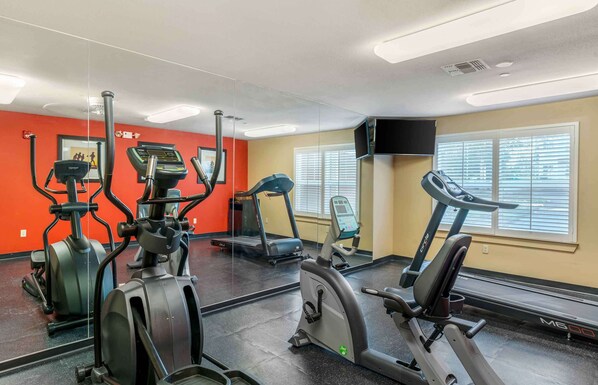 Une salle de sport équipée de machines de cardio, d’un tapis de course et d’un mur recouvert de miroirs.