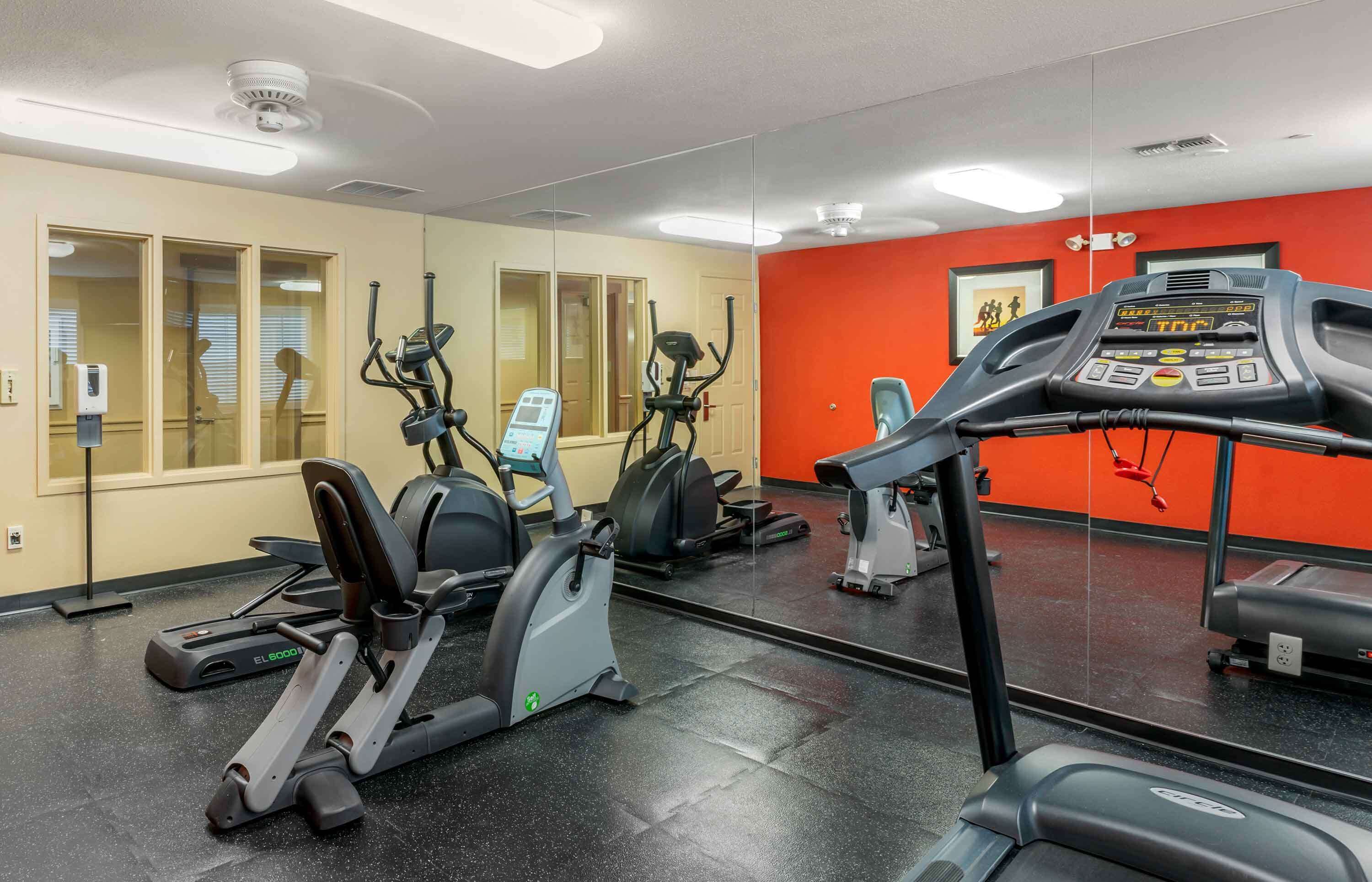 A gym with various exercise equipment, including treadmills and elliptical machines, and a large mirror on the wall.