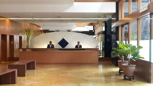 A reception area with a modern design, featuring a reception desk, two staff members, and a large potted plant.