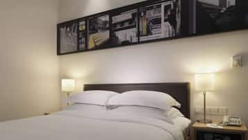 A hotel room with a bed, two bedside lamps, a nightstand with a phone, and a wall-mounted picture.