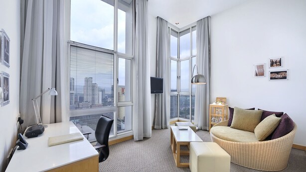 A modern hotel room with a large window, a desk with a computer, a comfortable sofa, and a small table.