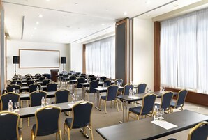 A conference room with rows of tables and chairs, a whiteboard, and large windows with curtains.