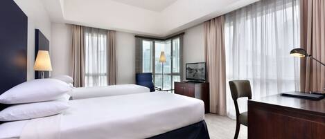 A hotel room with a large bed, a desk, a chair, and a television.