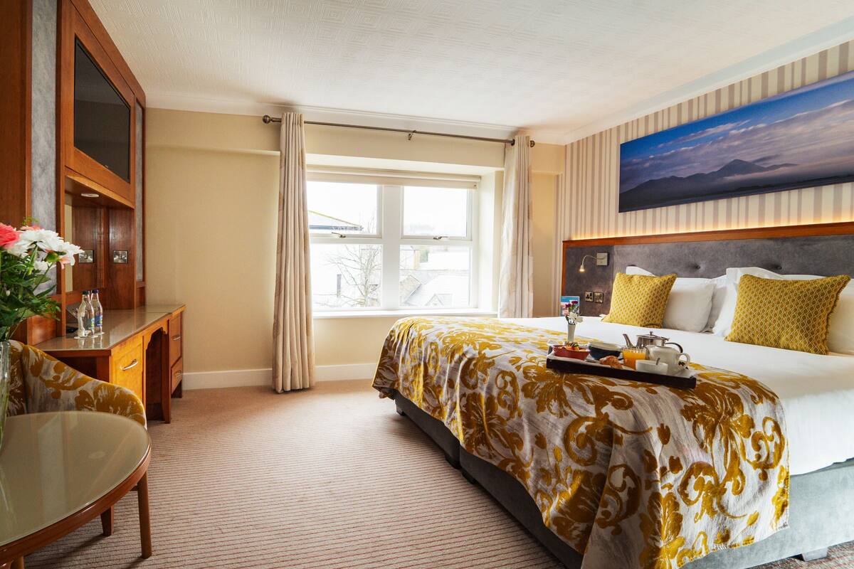 A hotel room with a bed, a desk, a chair, a window, and a painting on the wall.