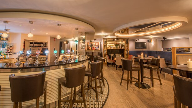 Zona de bar con una barra curva, varios taburetes y diferentes opciones de asientos, incluidas mesas y sillas.