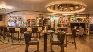 Zona de bar con distintas opciones de asientos, barra con varios tipos de botellas y un elemento decorativo circular en el techo.