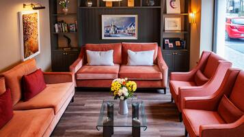 A modern living room with a sofa set, a glass coffee table with a vase of flowers, and a painting on the wall.