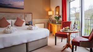 Habitación de hotel con cama, escritorio, silla, mesa con un florero y balcón con vistas.