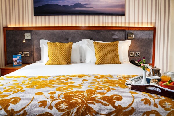Habitación de hotel con una cama grande, cabecera de madera y vistas a las montañas a través de la ventana.
