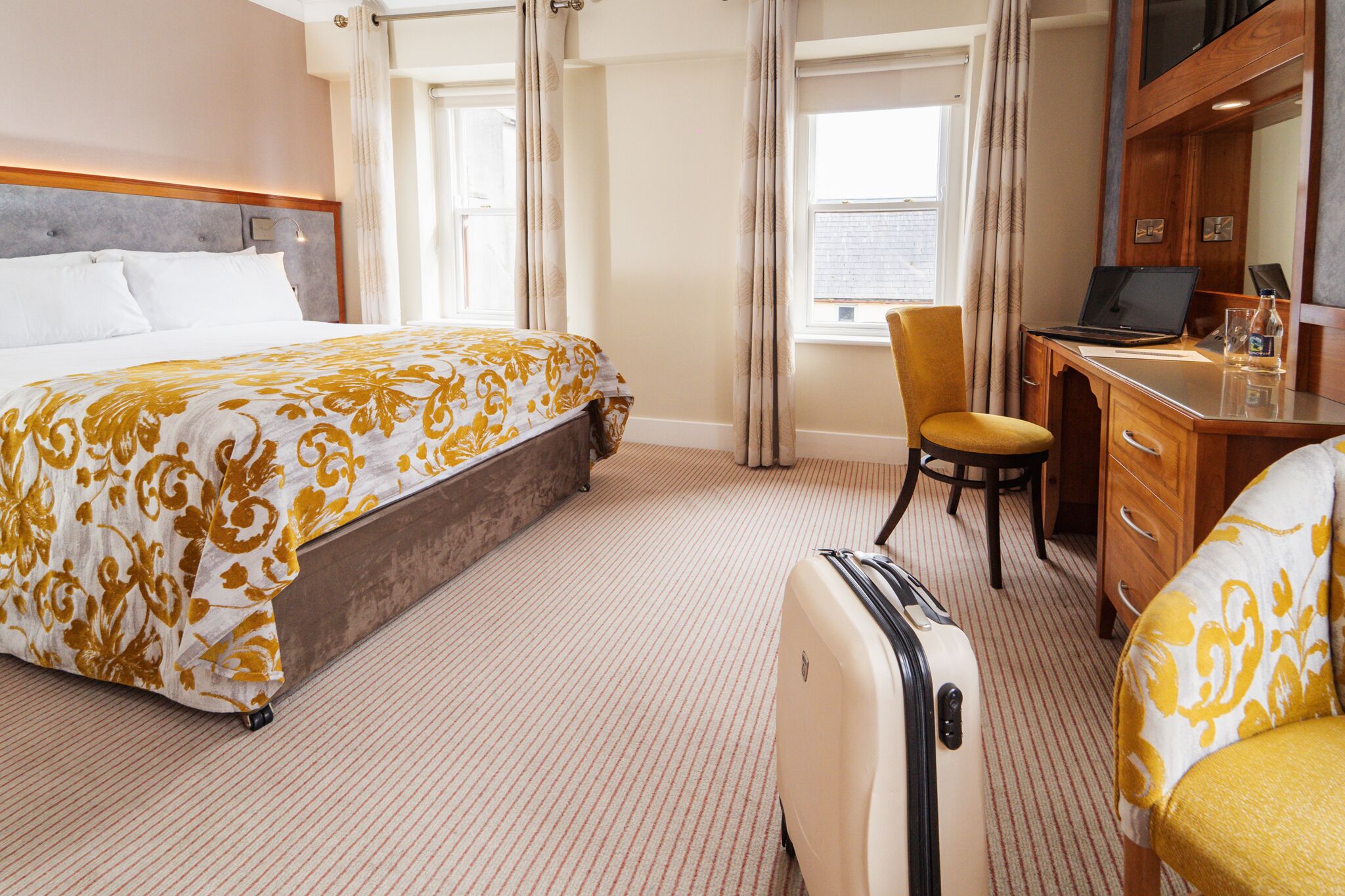 Una habitación de hotel con una cama, un escritorio, una silla y una maleta.