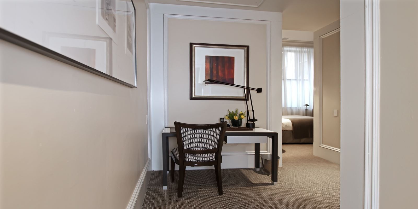 A hotel room with a desk, chair, and a framed picture on the wall.