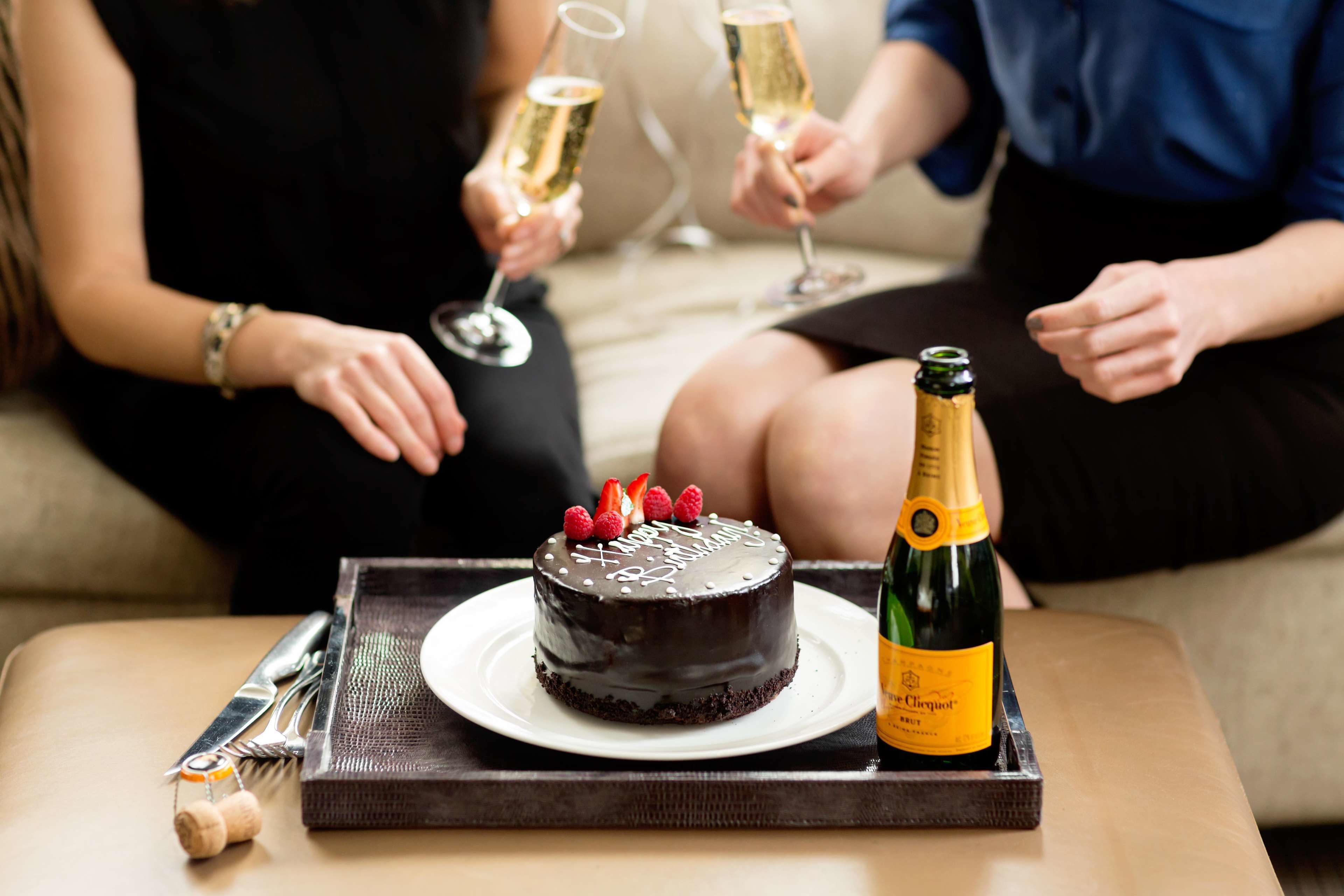 Een chocoladecake met aardbeien op een wit bord, een fles champagne, en een mes en vork op een schaal.