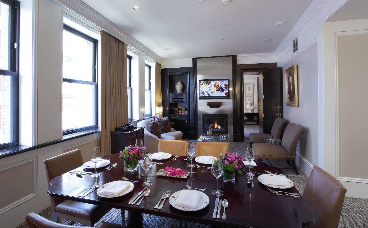 A dining area with a round table set for six, a fireplace, and a television in the background.