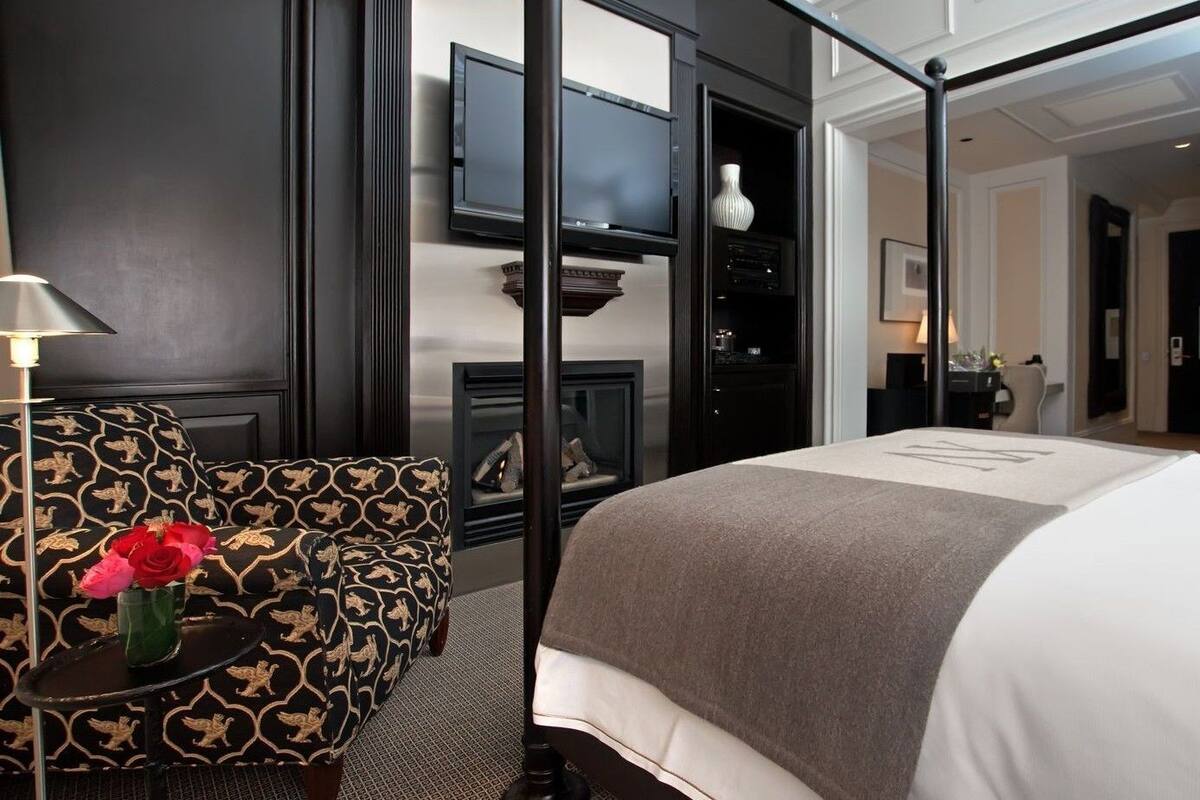 A hotel room with a bed, a sofa, a TV, and a fireplace.