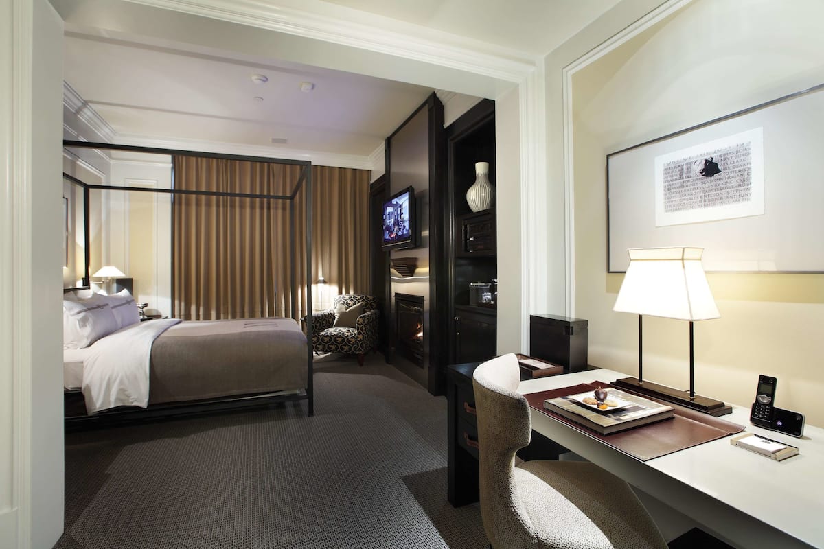 A hotel room with a bed, a desk with a lamp, a television, and a framed picture on the wall.