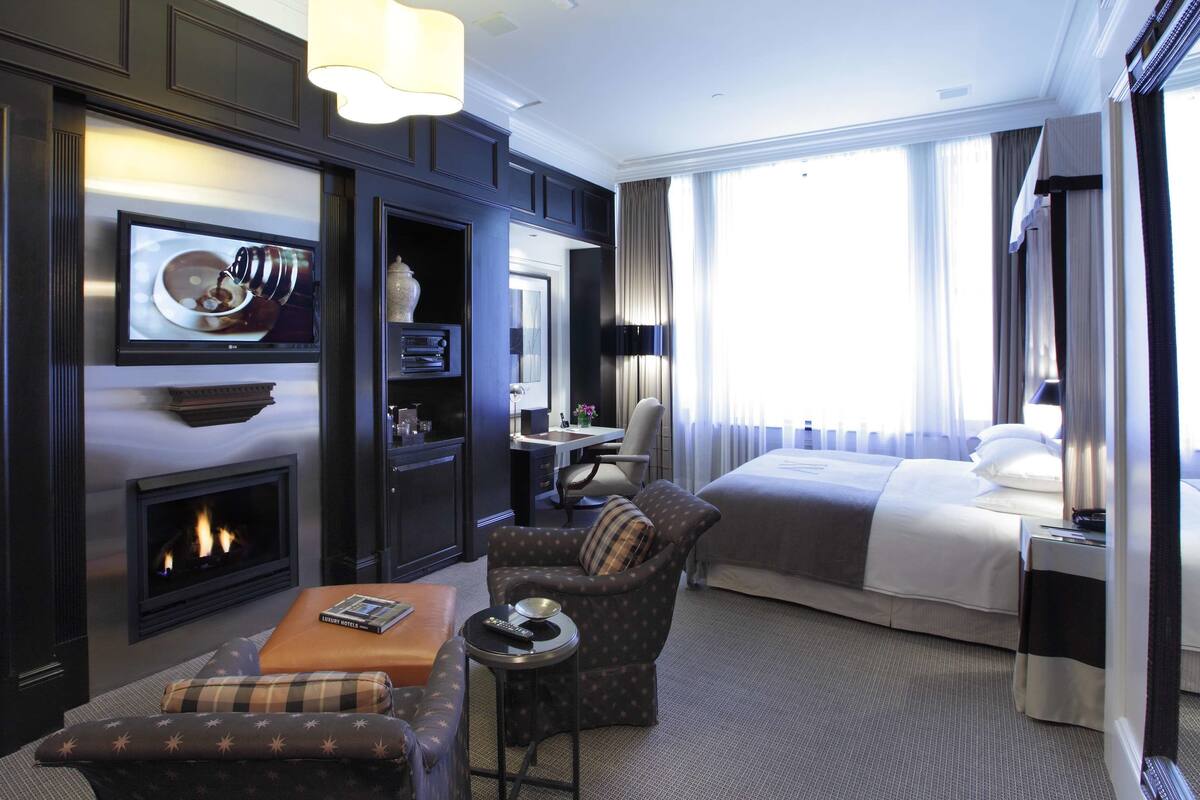 A hotel room with a fireplace, a bed, a desk, and a comfortable seating area.