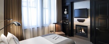 Een hotelkamer met een bed, een open haard, een aan de muur bevestigde televisie en een raam met gordijnen.