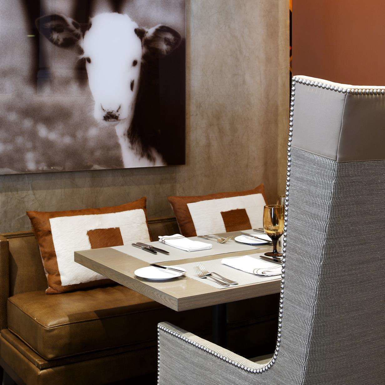 A restaurant setting with a booth seating arrangement, a table set for dining, and a wall-mounted painting of a cow.