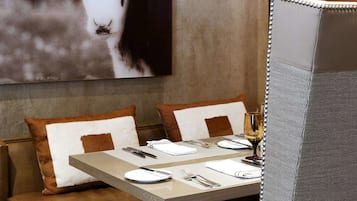 A restaurant setting with a booth seating arrangement, a table set for dining, and a wall-mounted painting of a cow.