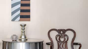 A room with a metallic side table, a decorative lamp, a striped wall hanging, and an ornate wooden chair.
