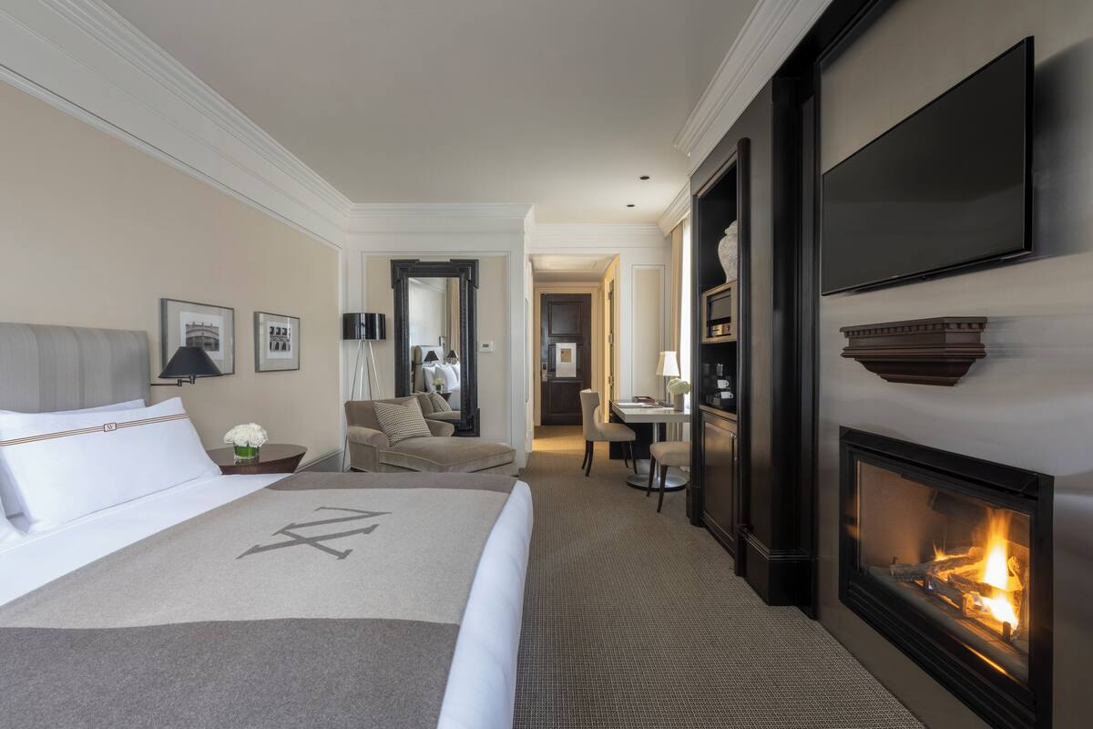 A hotel room with a bed, a fireplace, a desk, and a television.