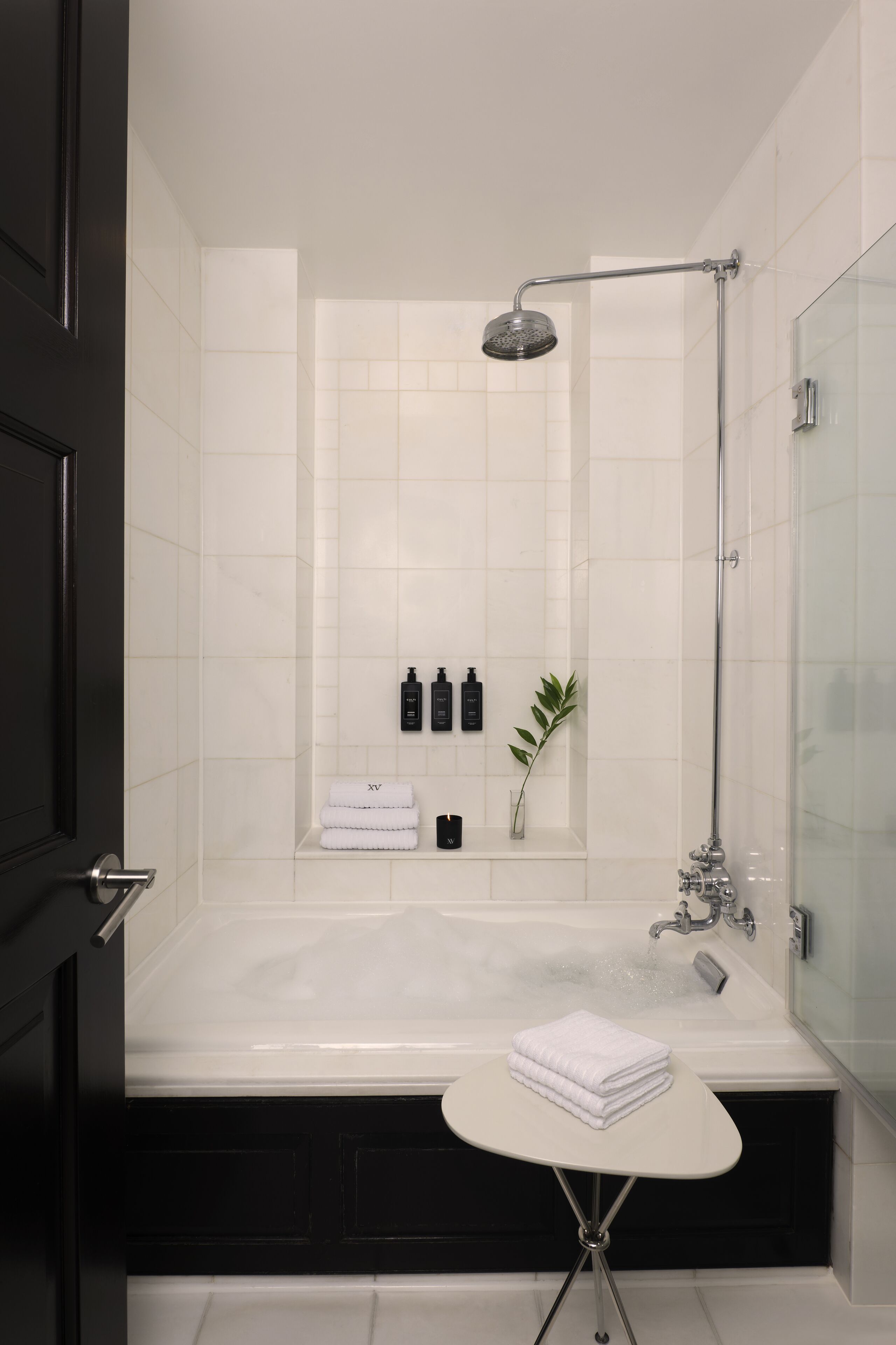 A modern bathroom with a large bathtub, a showerhead, and a small table with towels.