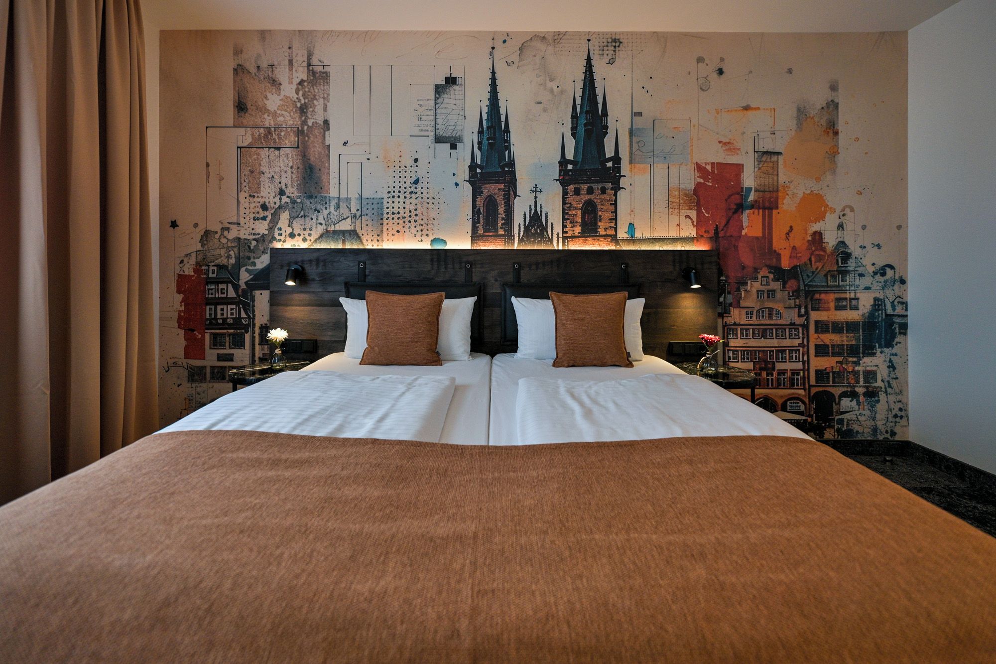 Ein Hotelzimmer mit einem großen Bett, zwei Kissen, einer Kopfteil und einem Stadtbild-Wandgemälde.