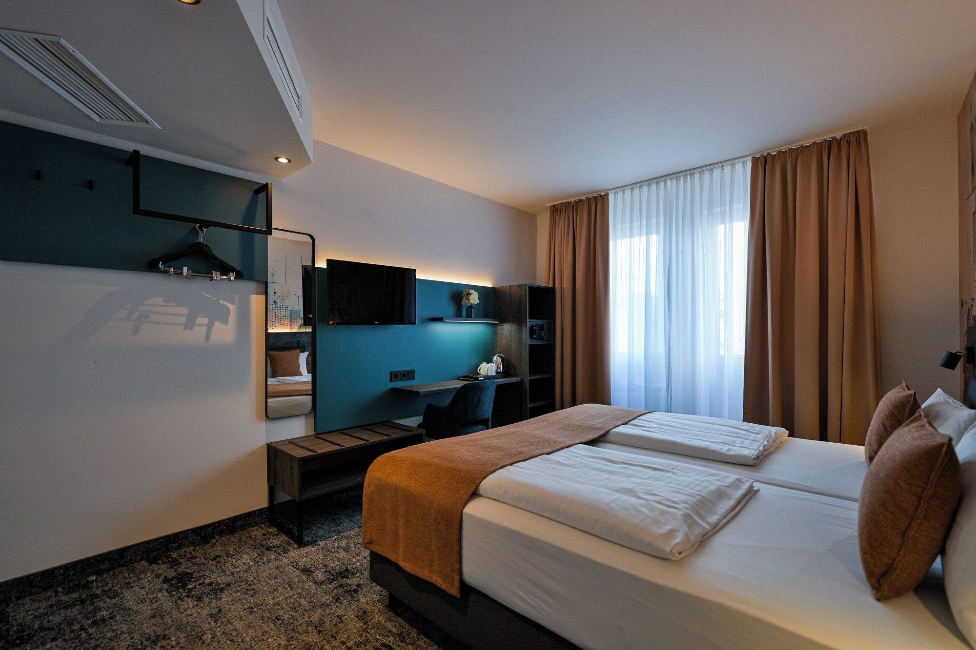 A hotel room with a bed, a desk, a chair, a mirror, and a window with curtains.