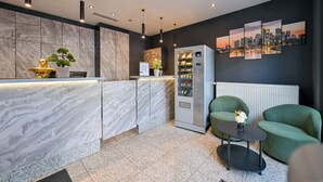 Un espace d’accueil moderne doté d’un comptoir de réception en marbre, d’un distributeur automatique et d’un coin salon avec des fauteuils à revêtement vert.