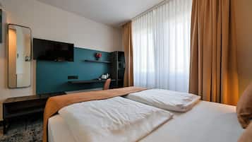 Ein Hotelzimmer mit Bett, Schreibtisch, Stuhl, Fernseher und einem Fenster mit Vorhängen.