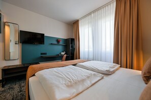 A hotel room with a bed, a desk, a chair, a TV, and a window with curtains. - Hotel Miramar Frankfurt City Centre (Frankfurt)