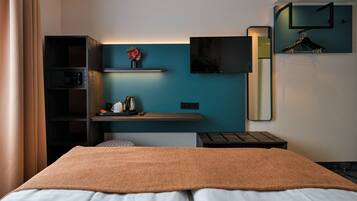 Una habitación de hotel con cama, escritorio con cafetera, televisor y espejo.