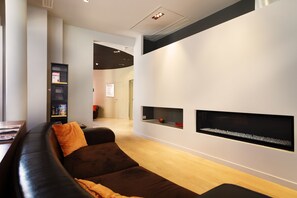 A modern living room with a dark brown sofa, a bookshelf, and two wall-mounted shelves with decorative items. - Hôtel Châteaudun Opéra (Paris)