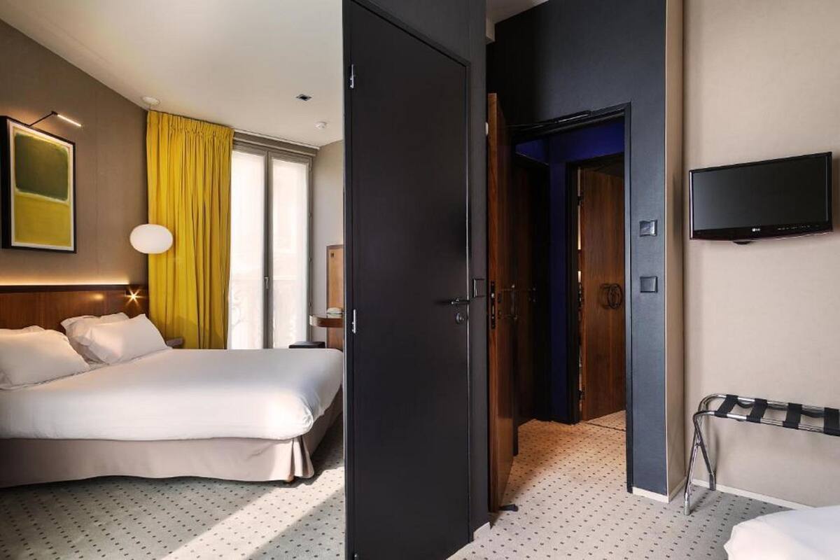 A hotel room with a bed, a TV mounted on the wall, and a door leading to another room.