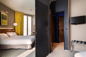 A hotel room with a bed, a TV mounted on the wall, and a door leading to another room. - Hôtel Châteaudun Opéra (Paris)