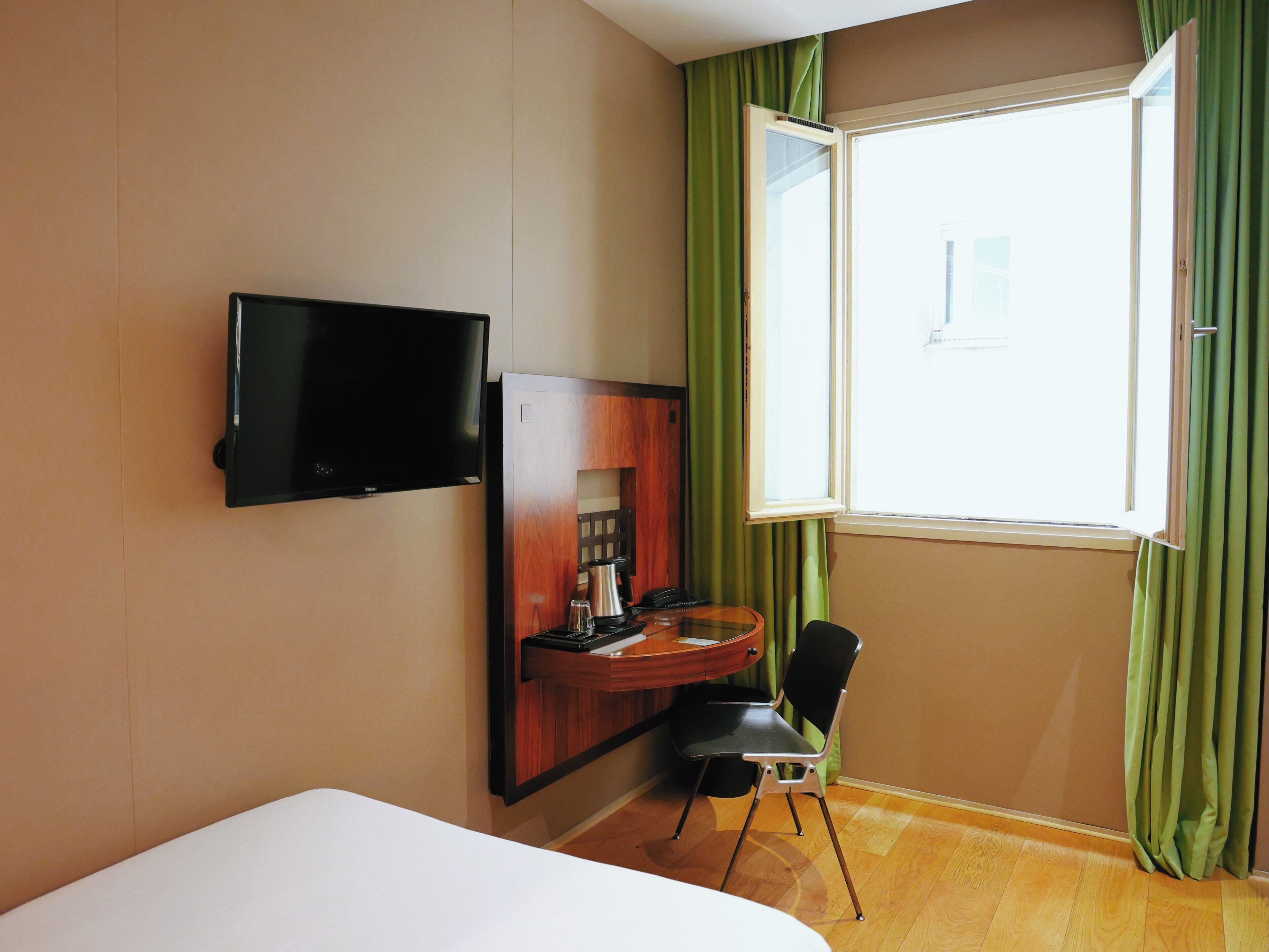 A hotel room with a bed, a desk with a chair, a television, and a window with curtains.