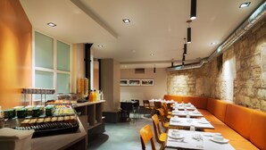 A restaurant with long tables, orange seating, and a buffet area with various food items. - Hôtel Châteaudun Opéra (Paris)